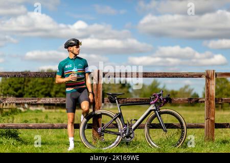 Radfahrer, der an einem Zaun lehnt, trinkt Stockfoto