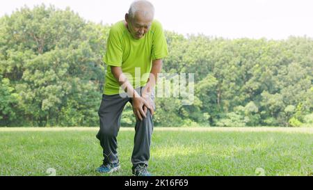 Der ältere Mann hat beim Laufen im Park Knieschmerzen Stockfoto