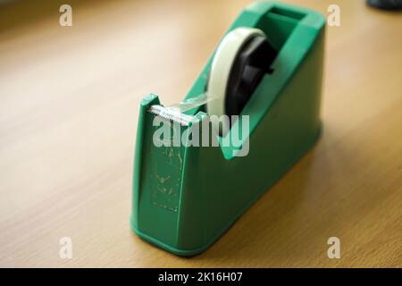 Grüner Bandspender mit transparentem Klebeband auf Holzhintergrund Stockfoto