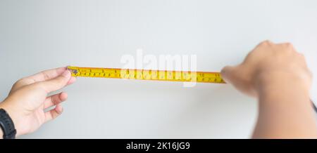 Mann Hand mit Maßband zum Messen mit Wandhintergründen zu Hause. DIY, Innenarchitektur, Reparatur und Verbesserung Haus oder Wohnung Konzepte Stockfoto