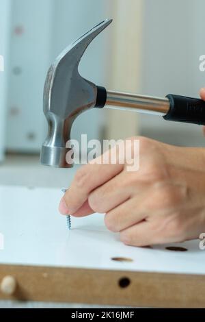 Mann mit Hammer hämmert einen Nagel in Holzbretter, Montage oder Reparatur von Möbeln zu Hause. DIY, Renovierung, Reparatur und Entwicklung nach Hause oder AP Stockfoto