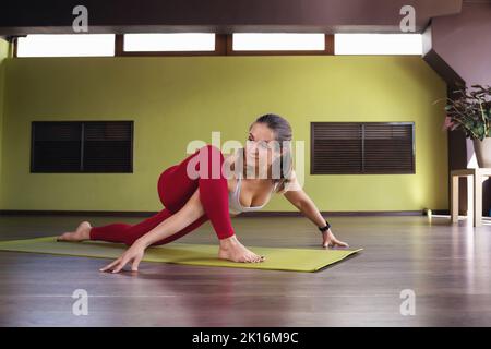 Frau, die Yoga praktiziert, Uttan Prishthasana trainiert, Eidechse posiert, im Studio auf Matte trainiert, gesundes Lifestyle-Konzept Stockfoto