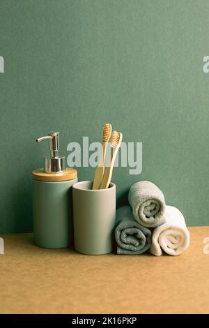 Seife, Shampoo-Flasche und Baumwollhandtücher, Zahnbürste auf braunem Regal. Grüner Wandhintergrund. Badezimmerausstattung Stockfoto