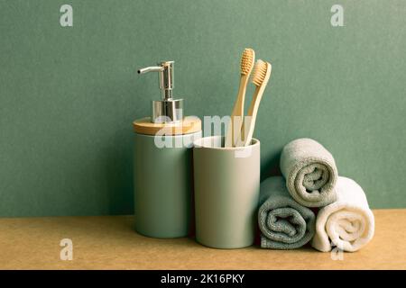 Seife, Shampoo-Flasche und Baumwollhandtücher, Zahnbürste auf braunem Regal. Grüner Wandhintergrund. Badezimmerausstattung Stockfoto