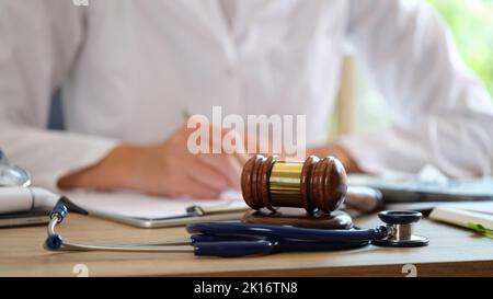 Gericht Gavel mit Stethoskop auf einem Tisch im Hintergrund Arzt schreibt Notizen Stockfoto