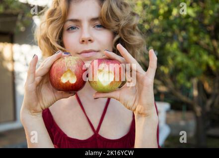 Schöne junge Frau von 18 - 20 Jahren hält zwei Äpfel in der Hand, in die Herzen eingeschnitzt sind. Konzentrieren Sie sich auf Äpfel. Richtige Vitamin-Ernährung, Ernährung. Surpri Stockfoto