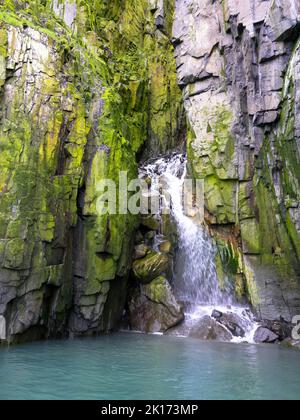 Spektakuläre Aussicht auf einen Wasserfall auf einem Gletscher. Die Vogelklippe Alkefjellet ist die berühmteste Klippe des Spitzbergen-Archipels. Hinloopen Fjord, Spitzbergen. Stockfoto