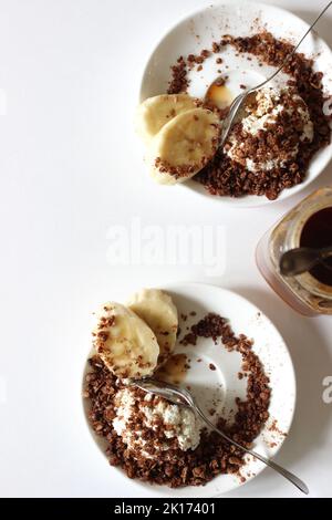 Zwei Teller mit Hüttenkäse mit hausgemachtem Müsli, Honig und Banane auf weißem Hintergrund. Gesundes Frühstück. Stockfoto