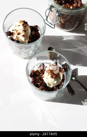 Hausgemachte Heidelbeeren-Granola mit Vanilleeis in Gläsern auf weißem Hintergrund serviert. Einfaches Dessert für Feiertage. Stockfoto