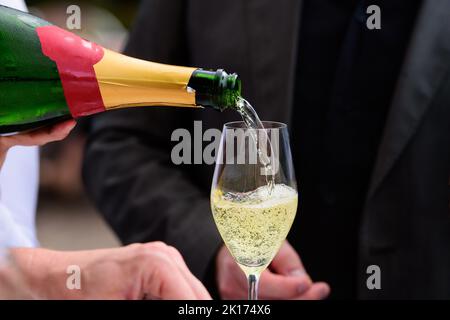 Nahaufnahme einer Champagnerflasche, die Champagner auf einer Sektflöte gegen eine verschwommene Person auf einer Party umschaufelt Stockfoto