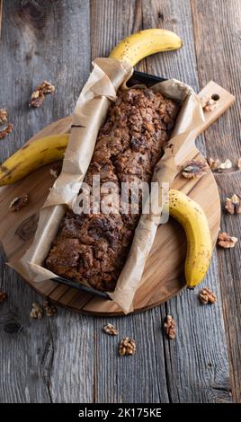 Laib frisches Bananbrot mit Walnüssen in einer auf einem Holztisch isolierten Backform Stockfoto