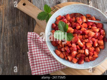 Gehackte Erdbeeren in einer Schüssel auf einem Holztisch Stockfoto