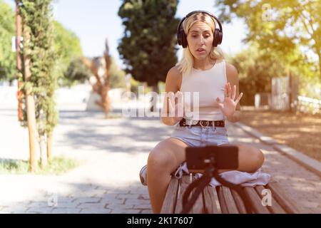 Influencer sendet live von einer Parkbank aus an ihre Follower. Konzept der Social Media Blogger, digitale Inhalte Schöpfer. Stockfoto