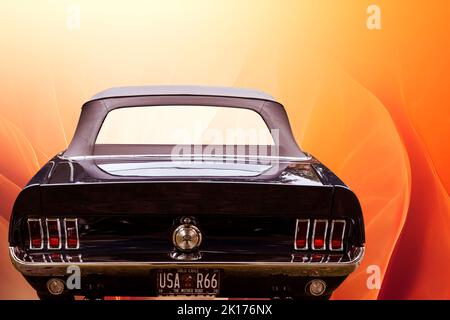 Ford Mustang Rückansicht eines dunkel lackierten amerikanischen Ponywagens vor surreal orangenen Hintergrund, Fahrzeugstandort Lehnin, Deutschland, 11. September 2022. Stockfoto