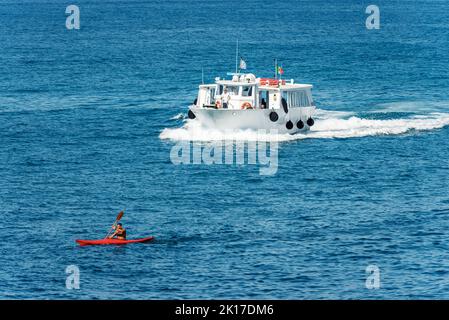 Fähre mit Touristen und einem erwachsenen Mann paddeln auf einem roten Kajak im blauen Mittelmeer. Tellaro Dorf, Lerici, Golf von La Spezia, Ligurien, Italien. Stockfoto