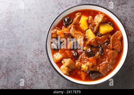 Khoresht Aloo schmorte Lammfleisch mit getrockneten Pflaumen oder Pflaumen, Tomaten, Zwiebeln, Kartoffeln, Karotten und Knoblauchzehen in der Schüssel auf dem Tisch. Horizontal oben V Stockfoto