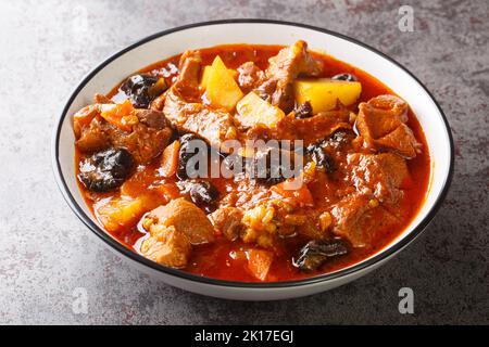 Khoresht Aloo schmorte Lammfleisch mit getrockneten Pflaumen oder Pflaumen, Tomaten, Zwiebeln, Kartoffeln, Karotten und Knoblauchzehen in der Schüssel auf dem Tisch. Horizontal Stockfoto