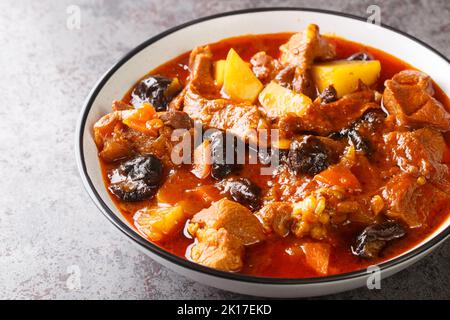 Pflaumeneintopf mit Lamm, Pflaumen, Tomaten, Karotten, Zwiebeln, Kartoffeln und Gewürze aus der Nähe auf einem Teller auf dem Tisch. Horizontal Stockfoto