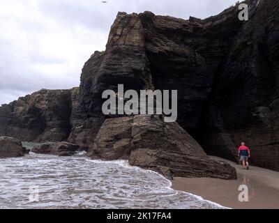 Rückansicht eines männlichen Touristen, der bei Ebbe in eine Strandhöhle eintauchen kann. Stockfoto