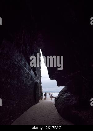 Touristen am Eingang einer Strandhöhle bei Ebbe. Stockfoto