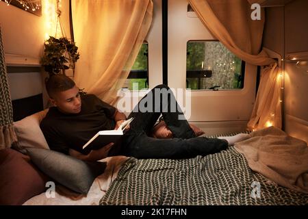 Mann liest Buch auf dem Bett im Wohnmobil Stockfoto