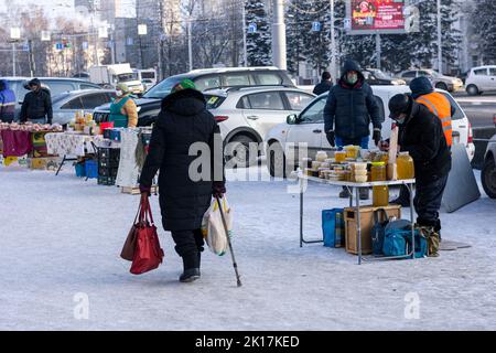 Die alte Frau mit einem Stock geht durch den traditionellen russischen Wintermarkt Stockfoto