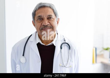 Porträt eines lächelnden, älteren biracial männlichen Arztes mit Stethoskop und weißem Mantel Stockfoto