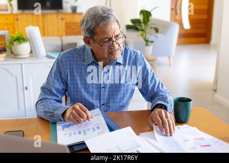 Seriöser leitender Geschäftsmann, der zu Hause an der Rezeption sitzt und sich den Papierkram ansieht Stockfoto