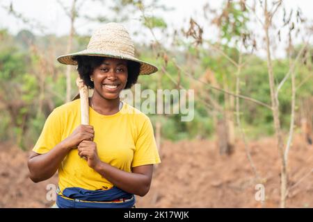 Glücklicher afrikanischer Bauer, der ihre Hacke hält Stockfoto