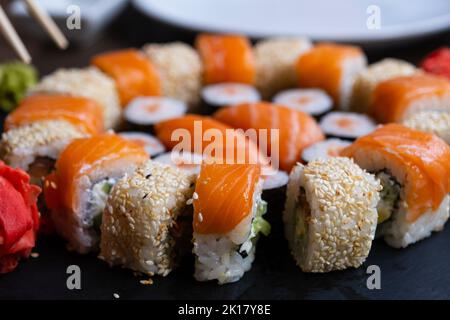Sushi auf dem Teller, Mittagessen im Restaurant. Set Sushi-Rolle mit Lachs, Avocado, Frischkäse, Gurke, Reis, Thunfisch auf dem schwarzen Teller Stockfoto