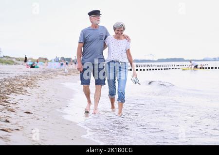 Rostock, Deutschland. 20. August 2022. ABBILDUNG - Ein pensionierter Pärchen geht Arm in Arm am Strand. Quelle: Annette Riedl/dpa/Alamy Live News Stockfoto