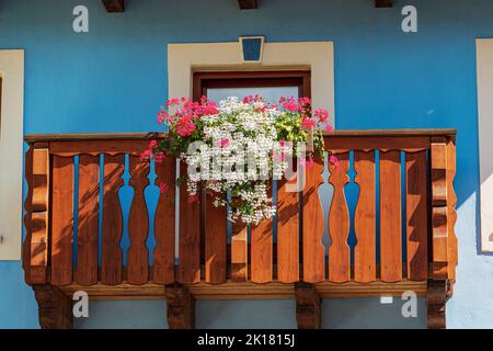 Holzbalkon mit weißen und roten Geranienblumen. Kleines Dorf von Malborghetto-Valbruna im Val Canale, Udine, Friaul-Julisch Venetien, Italien, Europa. Stockfoto