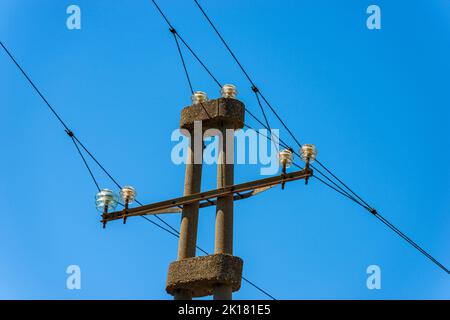 Nahaufnahme einer alten Betonsäule mit einer Stromleitung vor einem klaren blauen Himmel. Italien, Europa. Stockfoto