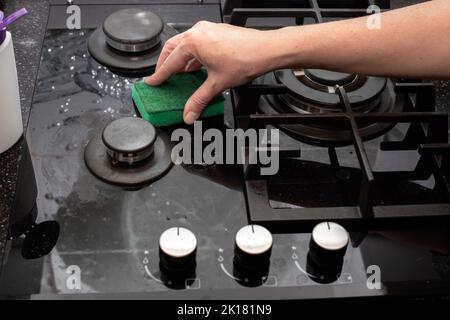 Eine Hausfrau reinigt den Gas-Glaskeramikherd mit einem Schwamm. Hausreinigung. Stockfoto