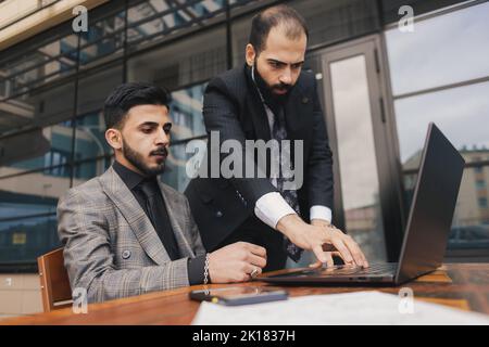 Geschäftsleute treffen sich im Freien. Zwei Männer benutzen einen Laptop. Arbeitspause. Team- und Business-Support. Zusammenarbeit und Partnerschaft Stockfoto