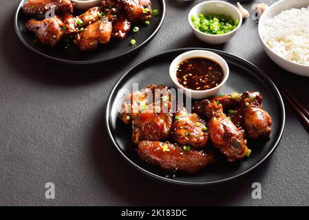 Klebrige Hähnchenflügel aus Honig und Soja auf dem Teller auf dunklem Steingrund. Stockfoto
