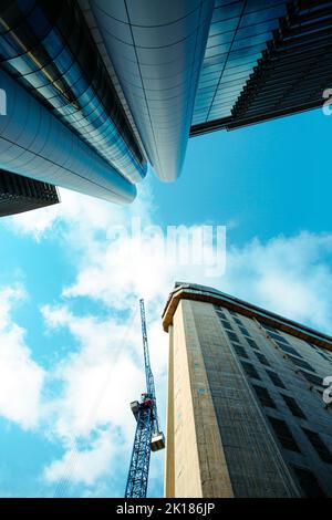 Ein Blick aus dem niedrigen Winkel auf einen neuen Wolkenkratzer, der gerade gebaut wird, mit einem Kran, der von Gebäuden mit Glasfassade im Stadtzentrum von Leeds umgeben ist Stockfoto