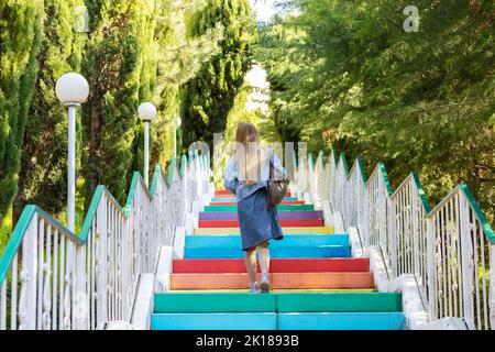 Eine Frau steigt farbige, bunte Treppen hinauf. Betonfarbene Stufen Stockfoto