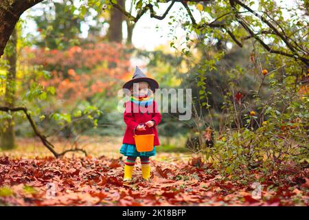 Kinder Trick or Treat in Halloween Kostüm. Kinder in bunten Kleidern mit Süßigkeiten Eimer auf Vorstadtstraße. Kleine Mädchen Trick oder Behandlung Stockfoto