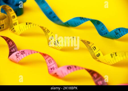 Rote, gelbe und blaue Messbänder auf gelbem Abdeckgrund. Konzept für Platz- und Gewichtsverlust kopieren. Stockfoto