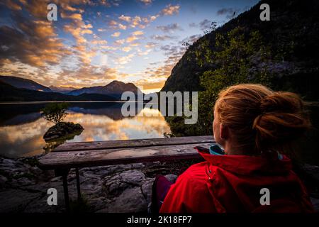 Weibliche Wanderin (im Fokus) genießen einen atemberaubenden Blick auf den alpinen Altausseer See im Ausseerland, Steiermark, Österreich, und einen atemberaubenden Sonnenuntergang Stockfoto