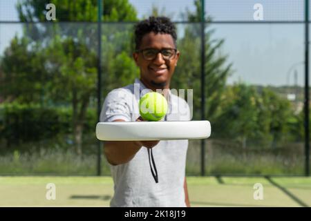 Schwarzer Tennisspieler balanciert Ball auf Schläger Stockfoto