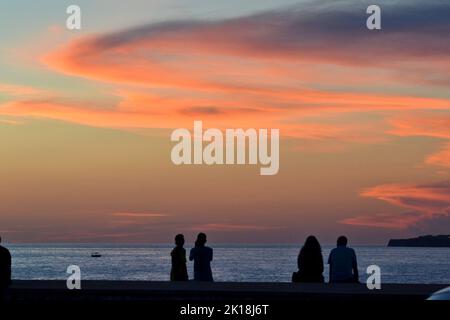 Sonnenuntergang in Cala Blanca, in der Nähe von Cuitadella, Menorca, mit Paaren, die gegen den Himmel geschildet sind Stockfoto