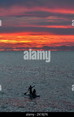 Sonnenuntergang in Cala Blanca, in der Nähe von Cuitadella, Menorca, mit einem Paar auf einem Stand-up-Paddleboard Stockfoto