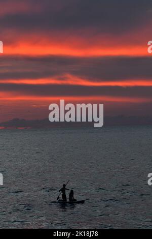 Sonnenuntergang in Cala Blanca, in der Nähe von Cuitadella, Menorca, mit einem Paar auf einem Stand-up-Paddleboard Stockfoto