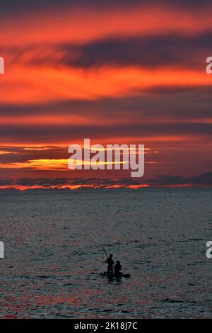 Sonnenuntergang in Cala Blanca, in der Nähe von Cuitadella, Menorca, mit einem Paar auf einem Stand-up-Paddleboard Stockfoto