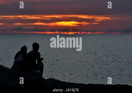 Sonnenuntergang in Cala Blanca, in der Nähe von Cuitadella, Menorca, mit Paaren, die gegen den Himmel geschildet sind Stockfoto