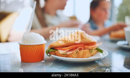 Eis und Croissant mit Fleisch vor dem Hintergrund der Menschen, die im Café essen. Stockfoto