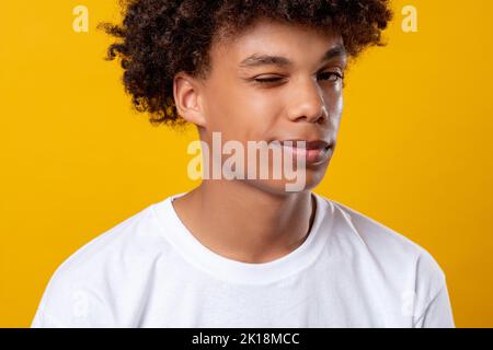 Schwarzes Teenager-Porträt. Positive Stimmung. Lächelnder afrikanischer Student, der die Kamera blinzelnd ansieht. Auf orangefarbenem Kopierbereich isoliert. Ethnische Toleranz. Konfi Stockfoto