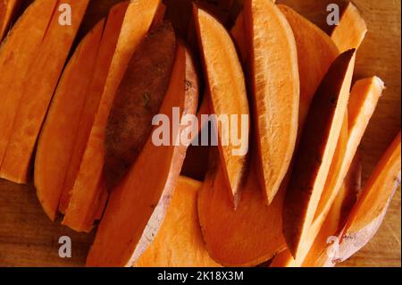 Flache Lay-Komposition mit geschnittenen Keilen von Süßkartoffeln auf Holztisch. Werbefläche kopieren. Gesundes, rohes veganes Essen. Banner Stockfoto